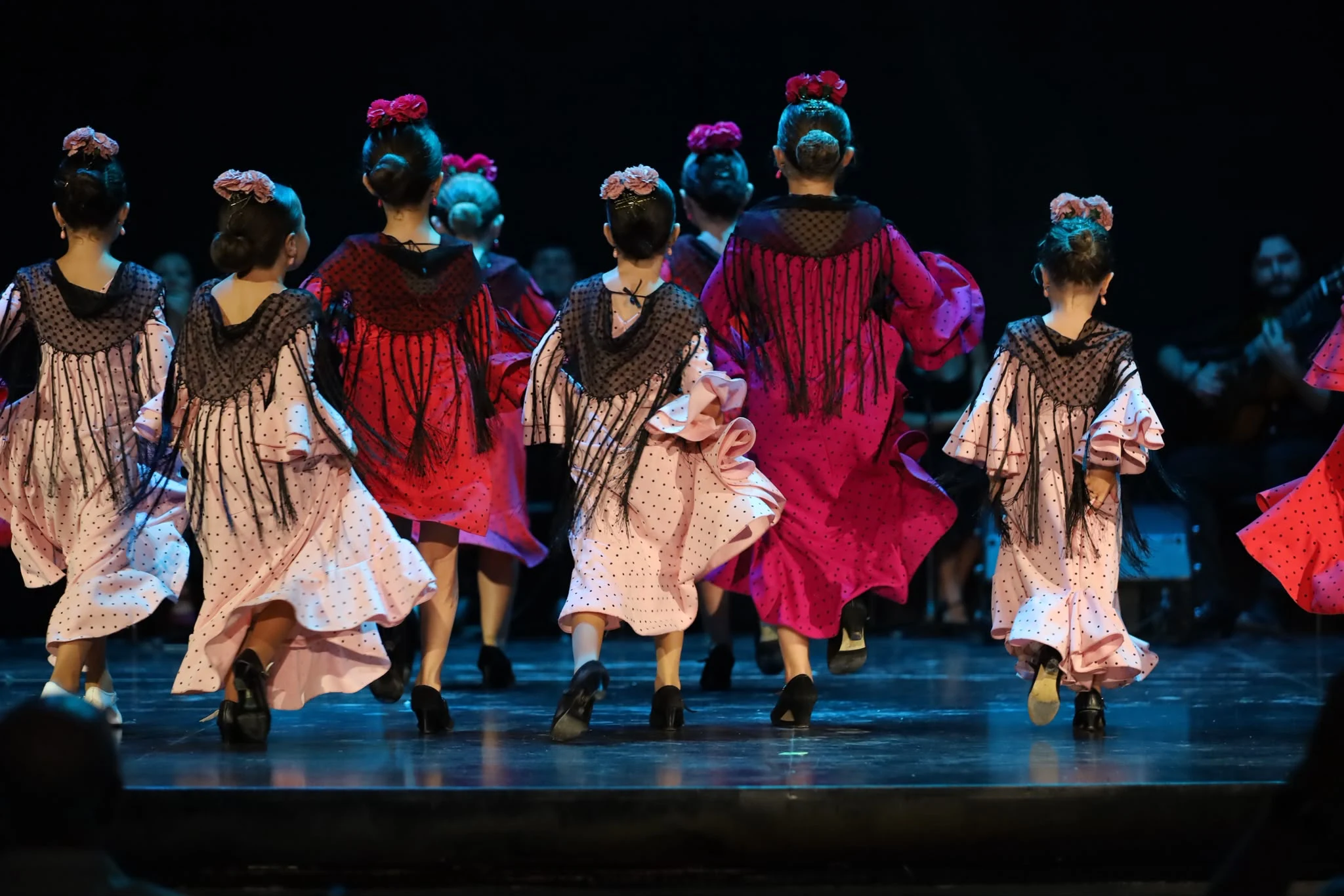 Grupo infantil de espaldas, con vestidos de flamenco sobre el escenario